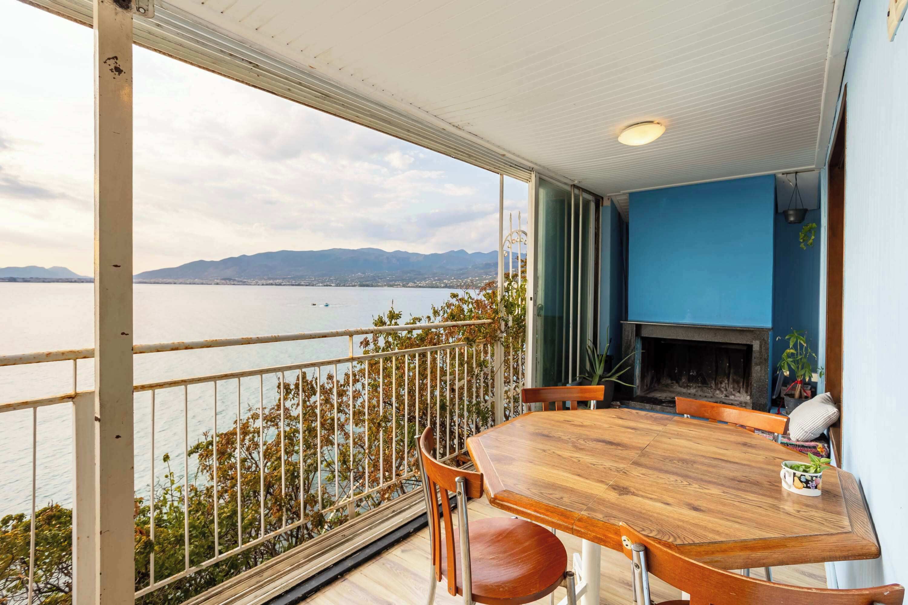 A balcony with a wooden table and chairs, a fireplace, and a view of a body of water and mountains.
