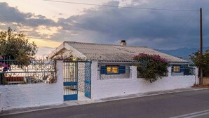 A white building with a blue gate and window shutters, surrounded by a fence and some vegetation. - Endless Blue Seafront Retreat - Mikra Mantineia (Paralia Vergas)