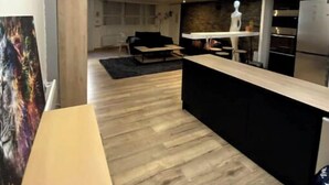 A modern kitchen with a wooden floor, a dining area with a table, and a living room with a sofa and a TV. - Loft Proche Centre Paris y Loger ou Professionnel (Suresnes)