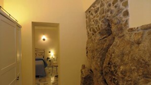 A narrow hallway with a bed and bedside table, a stone wall, and a door. - TERRAZZA DI ROSA-SEA VIEW (Praiano)