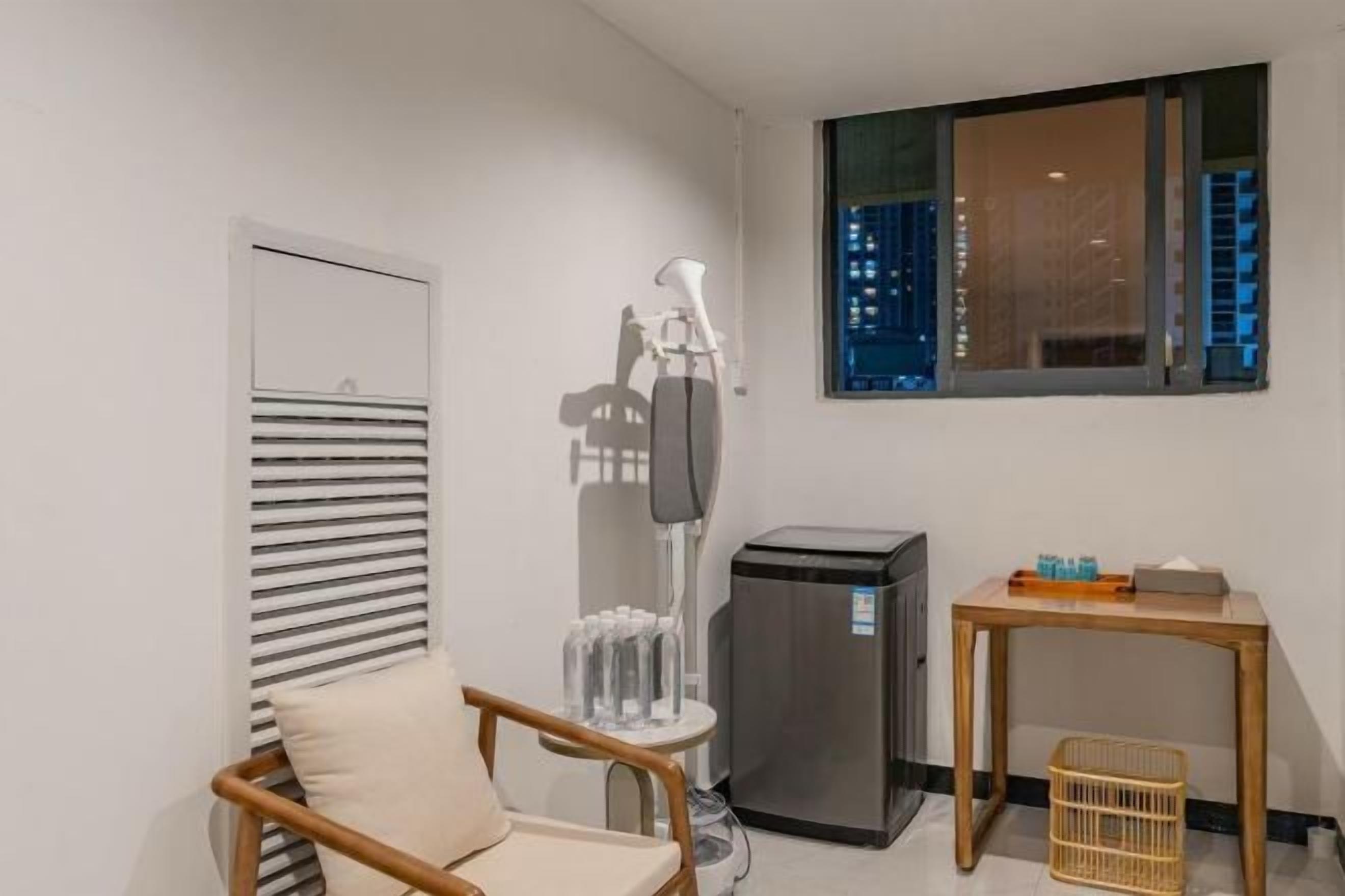 A small room with a chair, a table, a trash bin, and a window with a view of buildings.