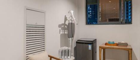 A small room with a chair, a table, a trash bin, and a window with a view of buildings.