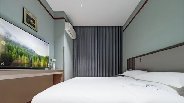 Habitación de hotel con cama, televisor de pantalla plana en la pared, ventana con cortinas y equipo de aire acondicionado.
