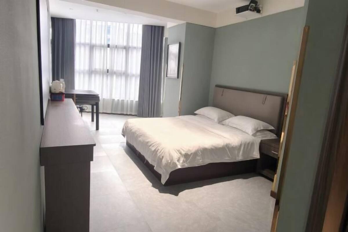 A hotel room with a bed, a desk, and a window with curtains.