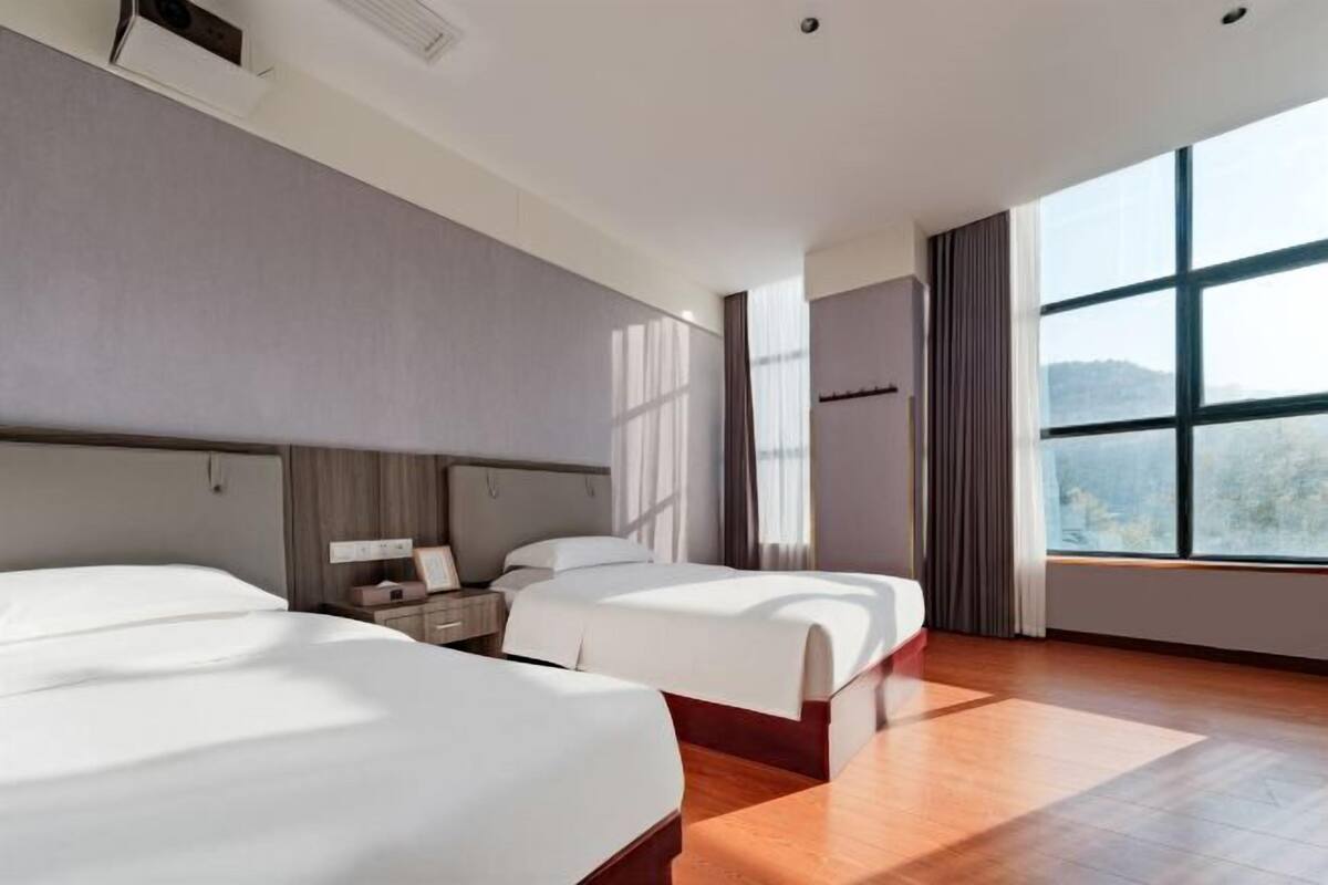 A hotel room with two beds, a large window, and a wooden floor.