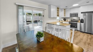 A modern kitchen with white cabinets, stainless steel appliances, and a wooden dining table with a plant centerpiece. - Wanna Go Back 3 Bedroom Home by RedAwning (Panama City Beach)
