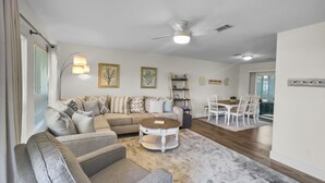 A spacious living room with a sectional sofa, a round coffee table, and a dining area with white chairs and a wooden table. - Wanna Go Back 3 Bedroom Home by RedAwning (Panama City Beach)