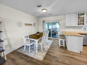 Una cocina moderna con armarios blancos, una mesa de comedor de madera y una pequeña isla con taburetes.