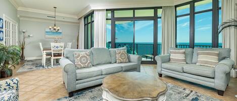A spacious living room with two grey sofas, a white coffee table, and a view of the ocean through large windows.
