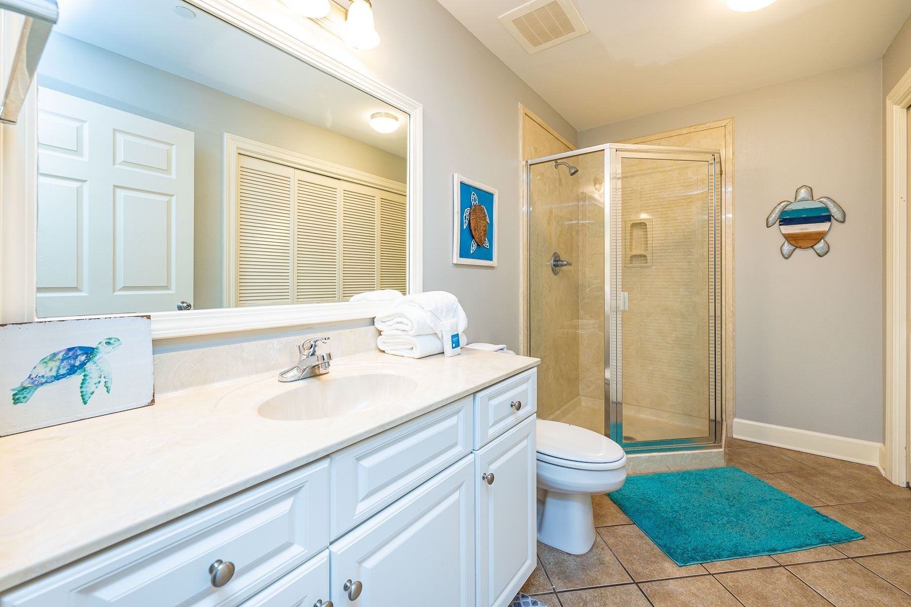 A bathroom with a white vanity, a sink, a toilet, a shower enclosure, and a blue rug.