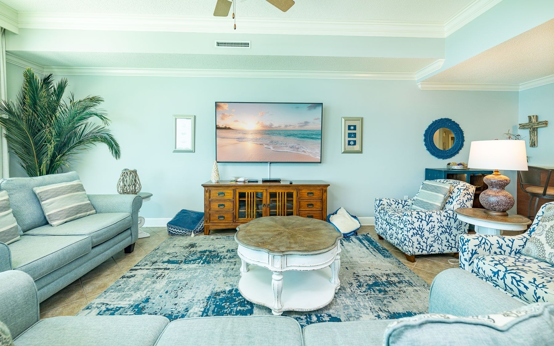 A living room with a sofa, ottoman, coffee table, and a television on a wall.