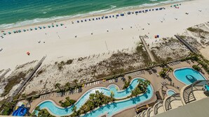 An aerial view of a beach resort with a swimming pool, beach umbrellas, and lounge chairs. - Phoenix West 1706 3 Bedroom Condo (Orange Beach)
