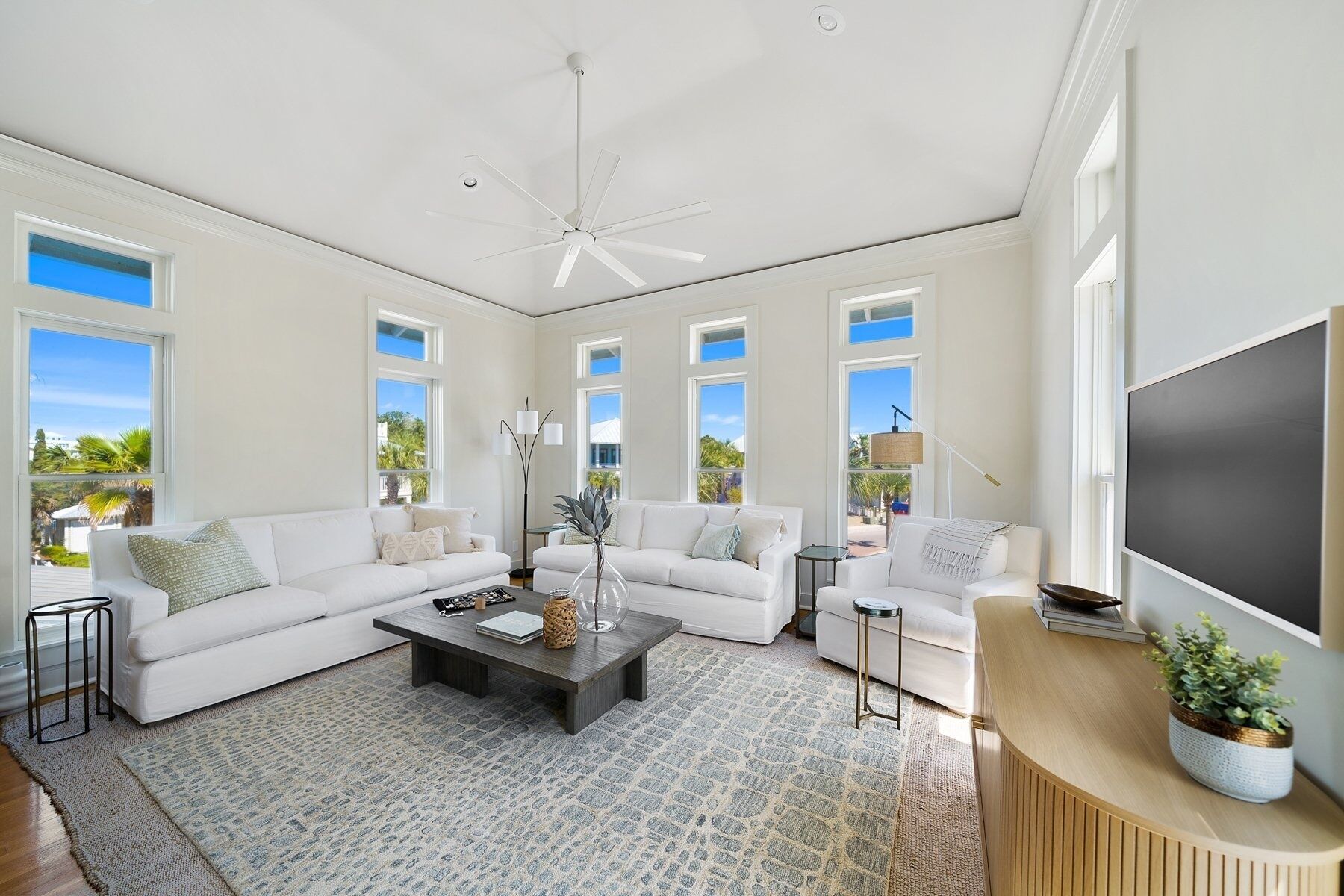 A spacious living room with a ceiling fan, large windows, and a flat-screen TV.