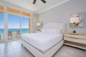 A hotel room with a large bed, a nightstand, a lamp, a painting, and a view of the ocean through a sliding door. - Phoenix Gulf Towers 808 4 Bedroom Condo (Orange Beach)