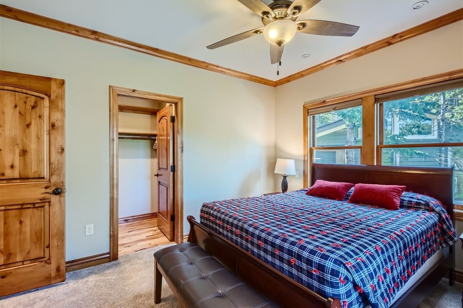 A bedroom with a bed, a bench, a ceiling fan, a window, and a door.