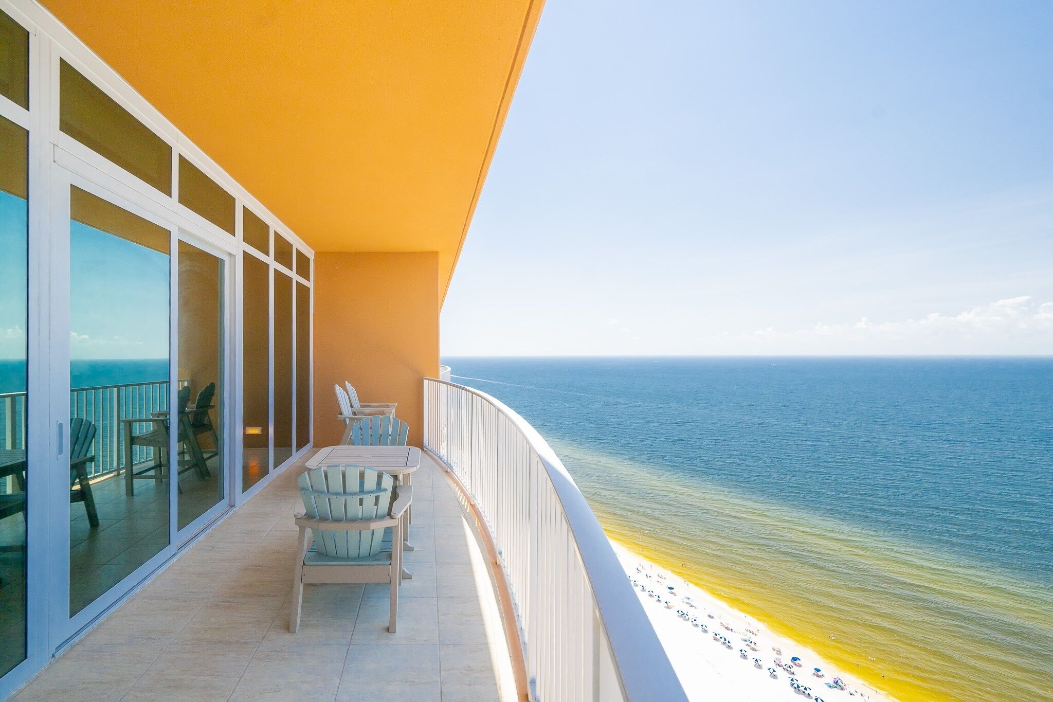 A balcony with a view of the ocean, a table with chairs, and a glass door leading to the interior.