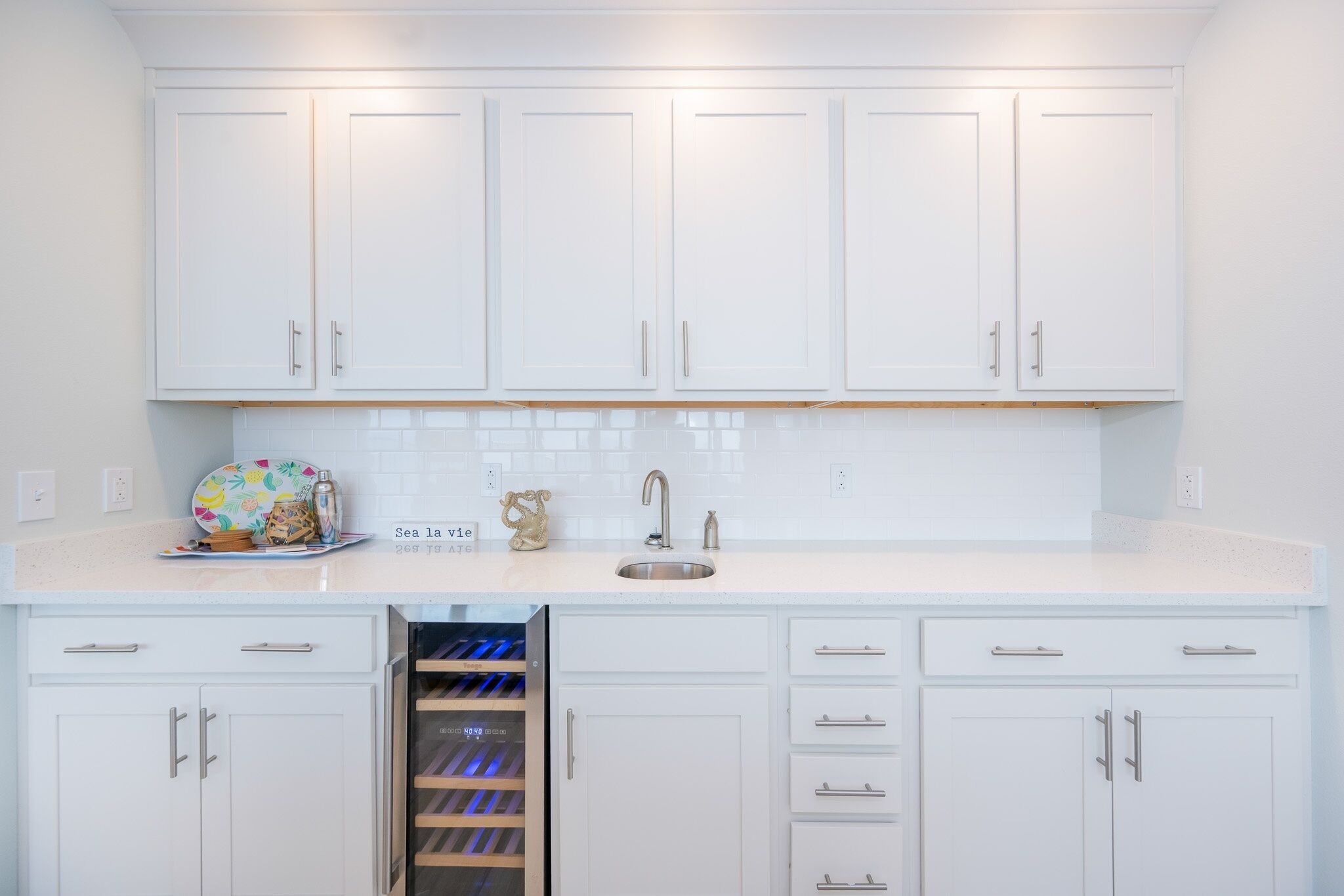 A kitchen with white cabinets, a stainless steel sink, and a built-in wine cooler.