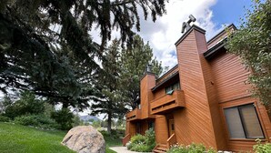 Una moderna casa in legno con un vialetto in pietra che conduce all'ingresso, immersa nel verde e circondata da grandi massi.