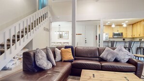 A living room with a brown leather sofa, a wooden coffee table, and a staircase with white railings.