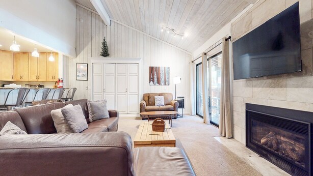A living room with a fireplace, a television mounted on the wall, and a dining area with chairs and a coffee station.