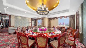 A hotel dining room with a round table, red upholstered chairs, and a chandelier.