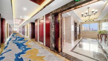 A hotel corridor with a carpeted floor, doors, and a chandelier.