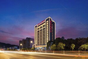 A multi-story hotel with illuminated signage, a well-lit facade, and a parking area in the foreground. - Xinlong Hotel (Wuhan)