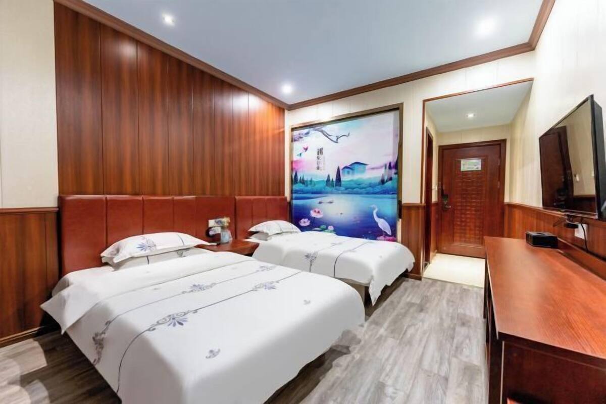 A hotel room with two beds, wooden paneling on the walls, a large painting, and a TV on a wooden desk.