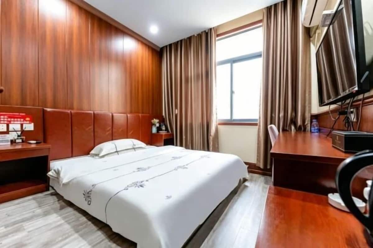 A hotel room with a bed, a desk, a chair, a TV, and a window with curtains.