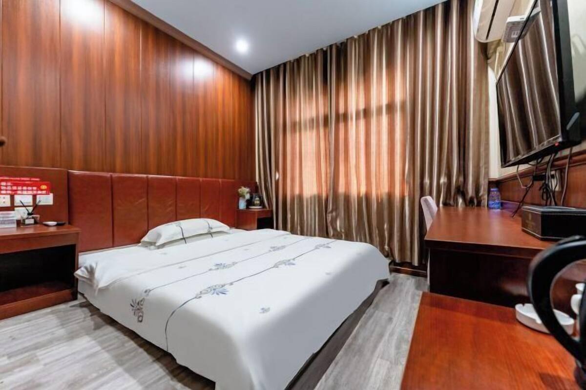 A hotel room with a bed, a desk, a chair, a TV, and curtains.