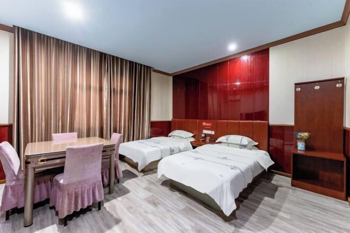 A hotel room with a wooden dining table, two beds, and a wardrobe.