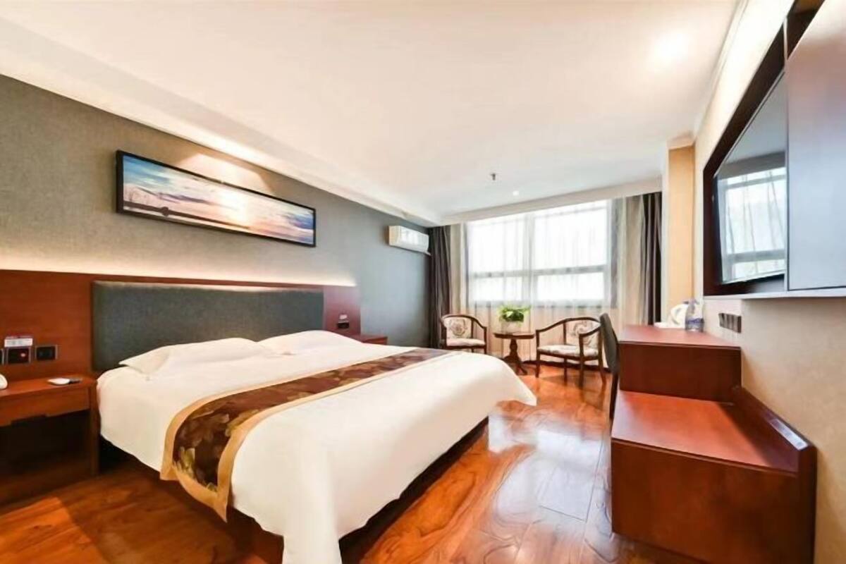 A hotel room with a bed, a desk, a chair, a TV, and a window.