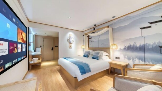 Una habitación de hotel moderna con una cama grande, mesitas de noche, un televisor montado en la pared y un mural con vistas panorámicas.