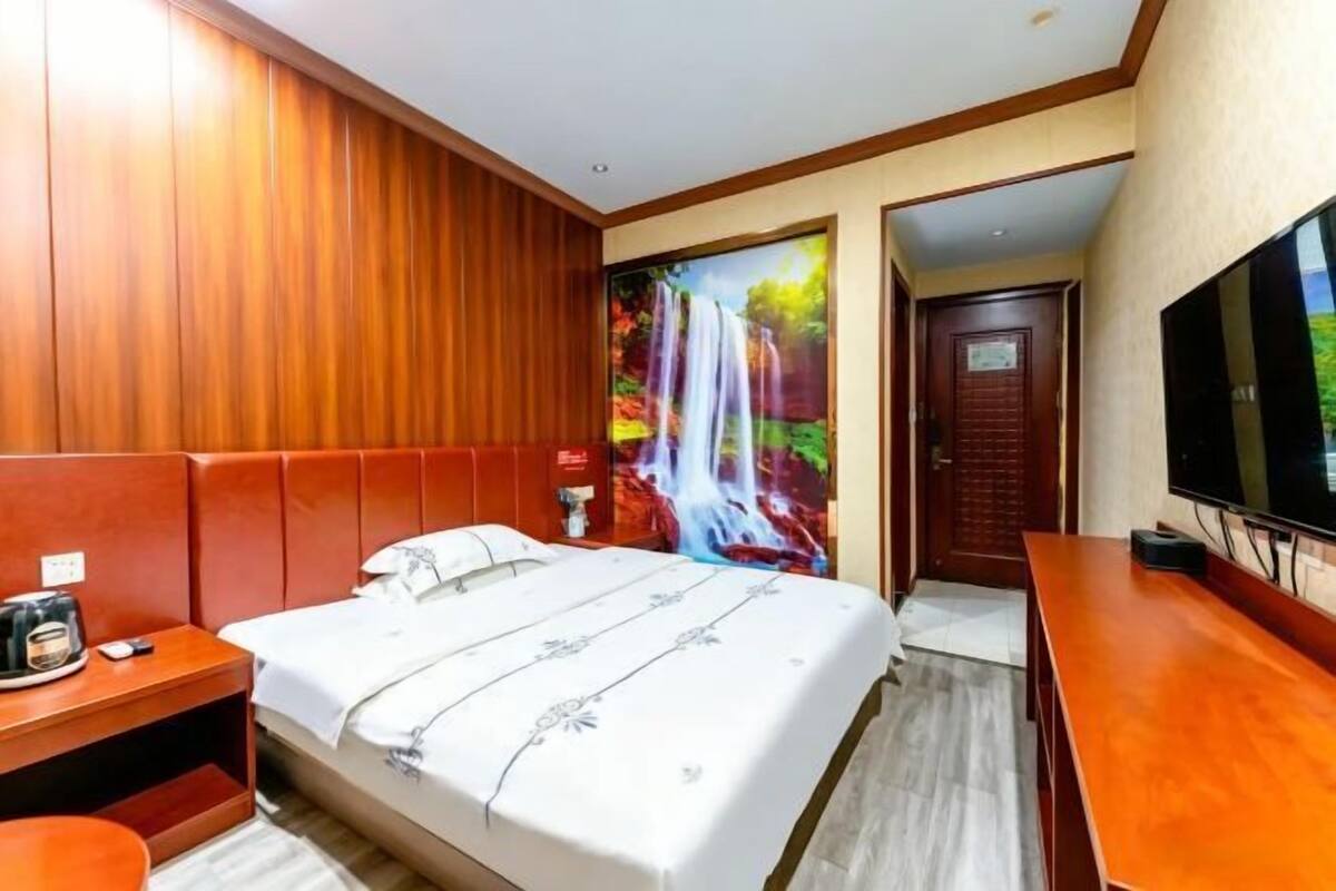 A hotel room with a bed, a desk, a TV, and a door.