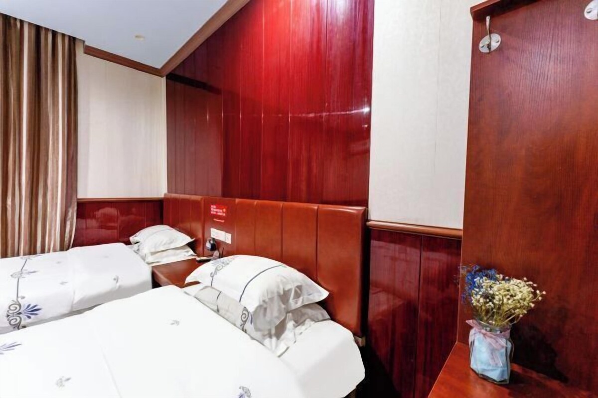 A hotel room with two beds, wooden paneling, a wooden door, and a vase with flowers on a nightstand.