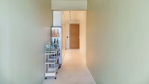 A narrow hallway with a white cart containing bottles and flowers, leading to a wooden door. - Uefio - Luxury Suites (Monte di Procida)