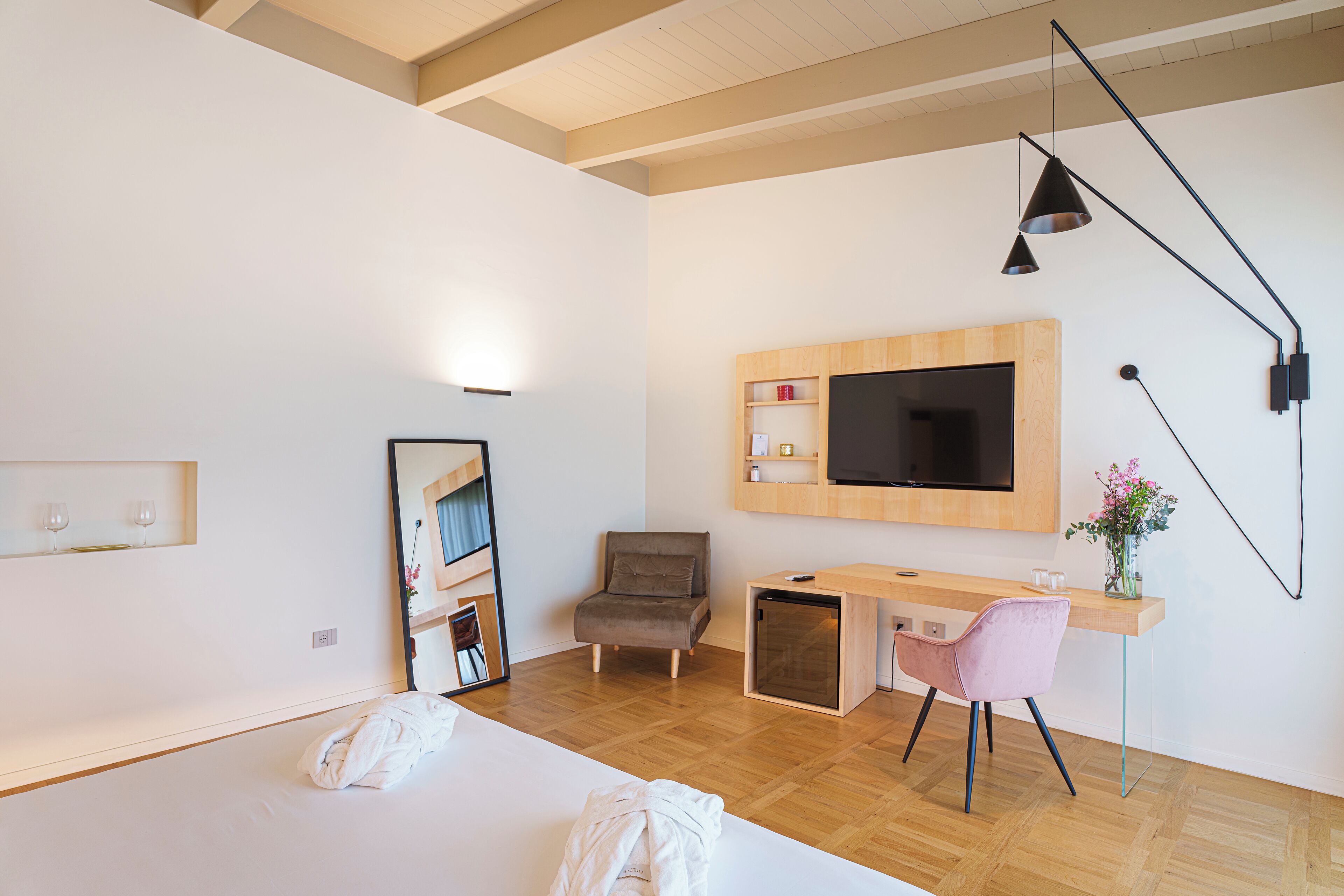 Quarto de hotel moderno com uma cama, uma escrivaninha com cadeira, uma televisão e um espelho.