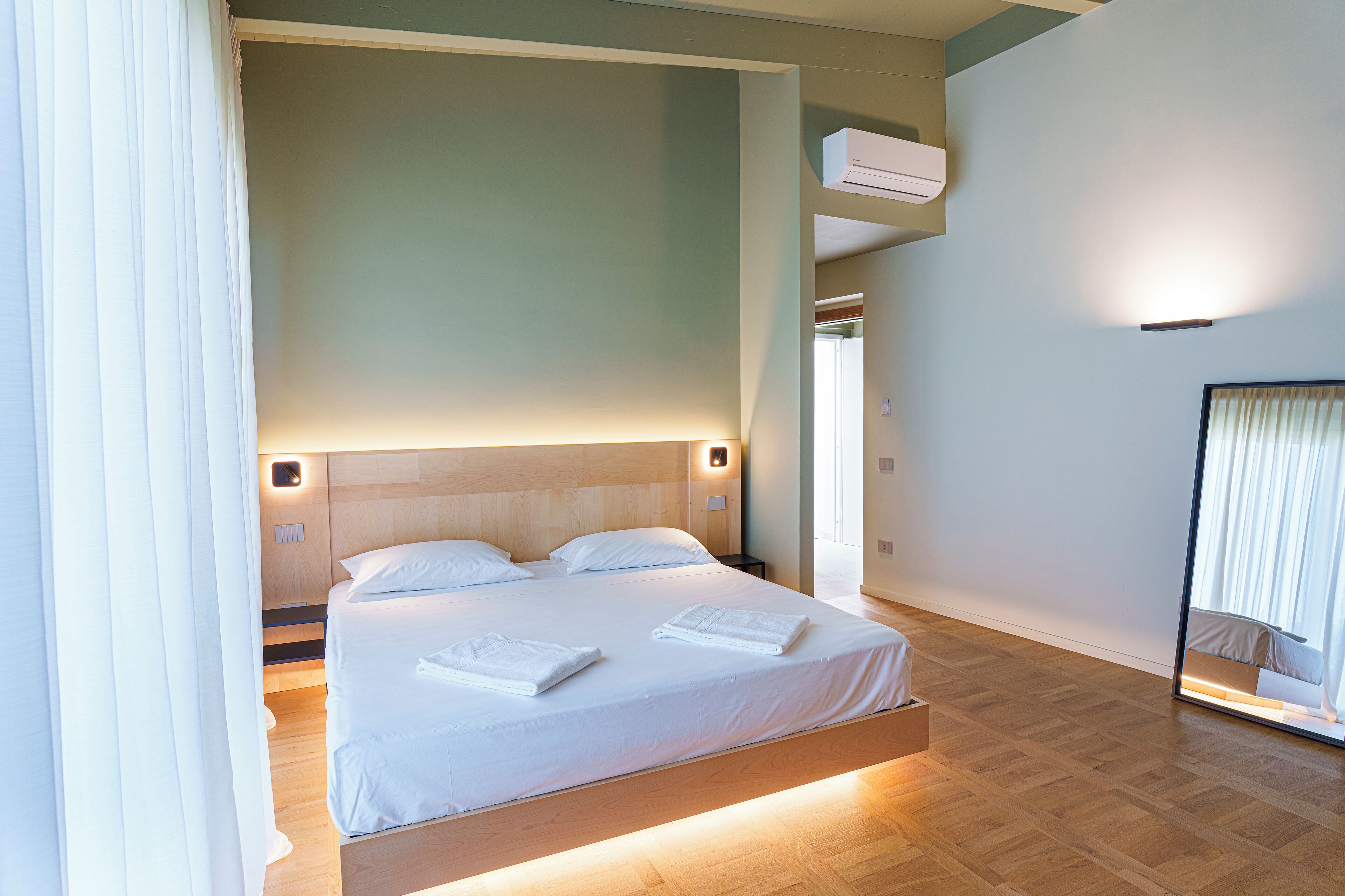 Una habitación de hotel moderna con una cama grande, cabecero de madera y un armario empotrado.