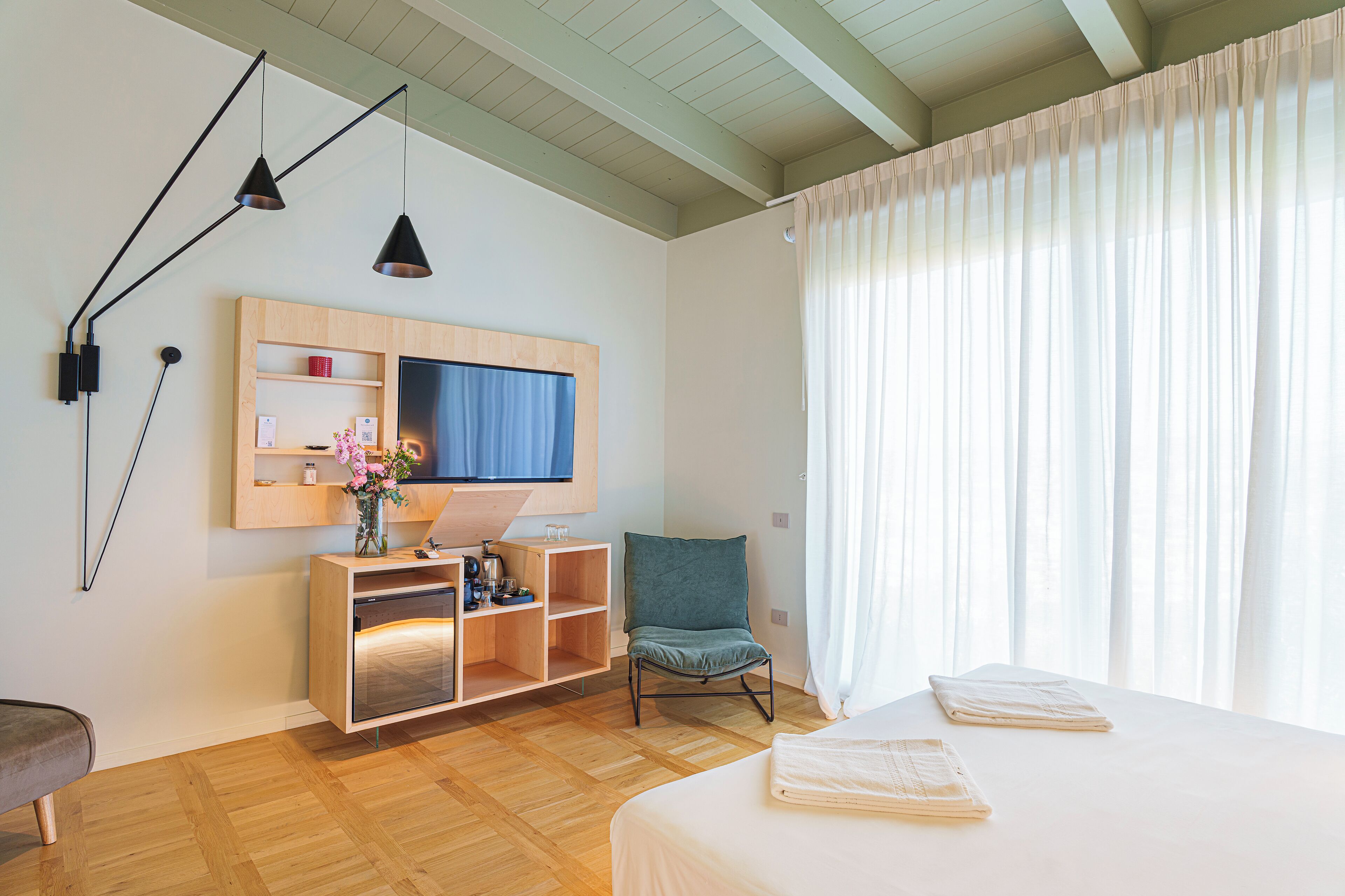 Un dormitorio con cama, televisor, armario de madera, silla y ventana con cortinas.