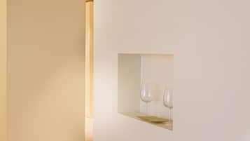 Un interior minimalista con pared blanca y un pequeño nicho que contiene dos copas de vino y una bandeja dorada.