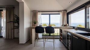 A modern kitchen with a large window, two black bar stools, and a view of the outdoors.