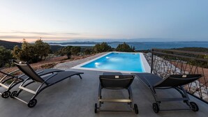 A pool with lounge chairs and a scenic view of the sea and mountains.