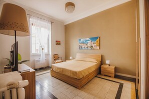 Une chambre à coucher comprenant un lit, des tables de chevet, un bureau avec une lampe, une chaise et une fenêtre avec des rideaux.