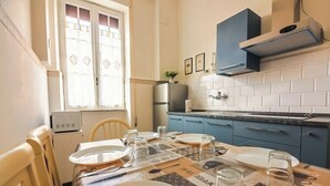 A dining area with a table set for four, a refrigerator, and a microwave in the background. - Grazioli Vatican Home (Roma)