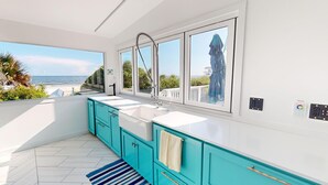 Une cuisine moderne dotée d’une grande fenêtre, de plans de travail blancs et d’armoires de couleur turquoise.