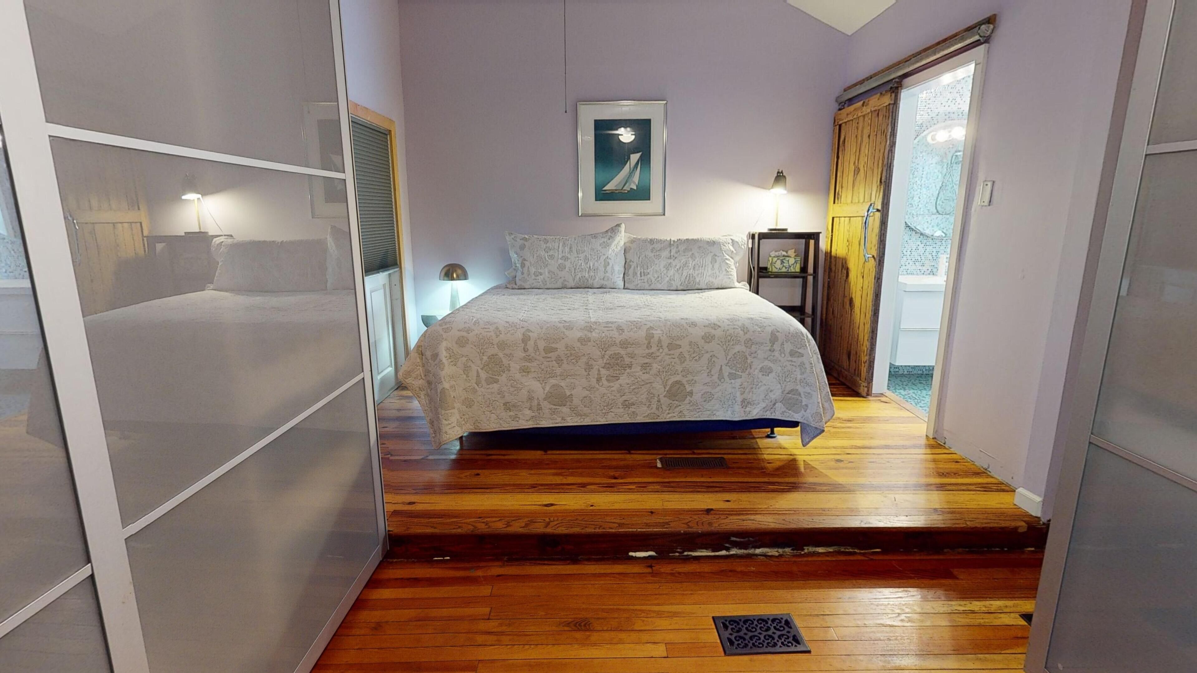 Ein Schlafzimmer mit einem Bett, einem Nachttisch, einem gerahmten Bild an der Wand und Holzboden.