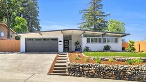 Una casa moderna de un solo nivel con garaje, un porche cubierto y un jardín delantero bien cuidado con un borde de piedra y plantas pequeñas.