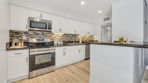 Una cocina moderna con armarios blancos, un horno de acero inoxidable, un microondas y un salpicadero de azulejos.