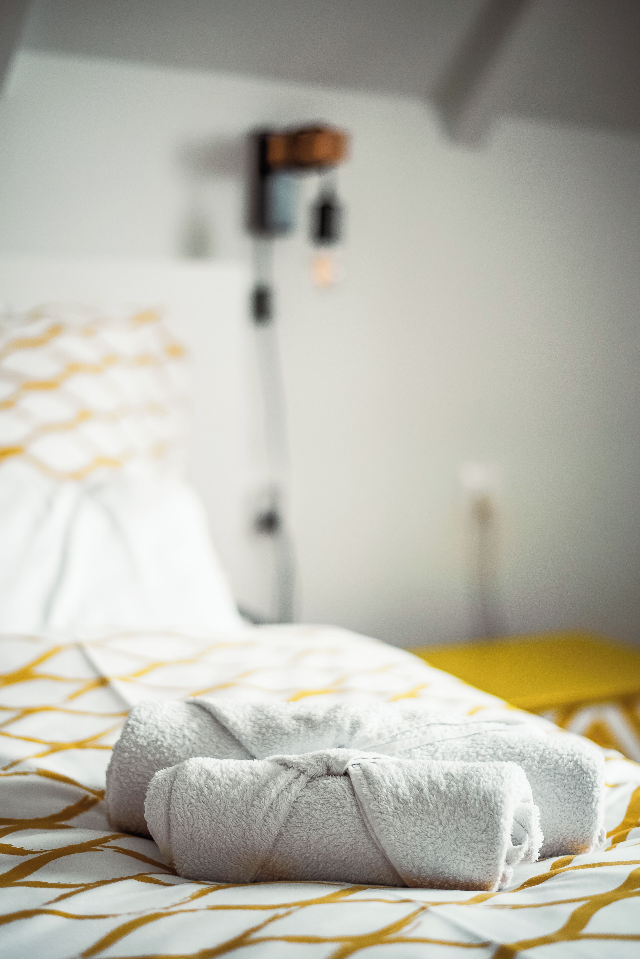 Een opgemaakt bed met een beddekleed met dessin en twee opgerolde handdoeken.