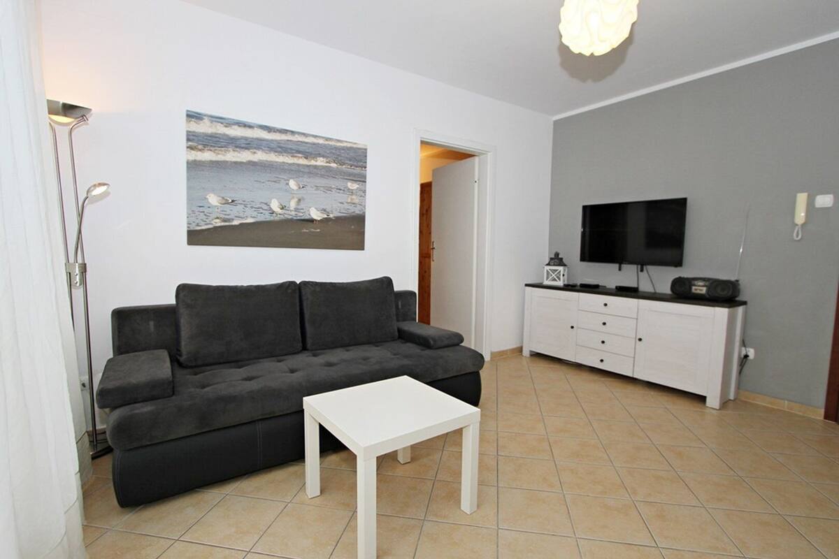 A living room with a dark grey sofa, a white coffee table, a flat-screen TV on a white cabinet, and a painting of a beach scene.